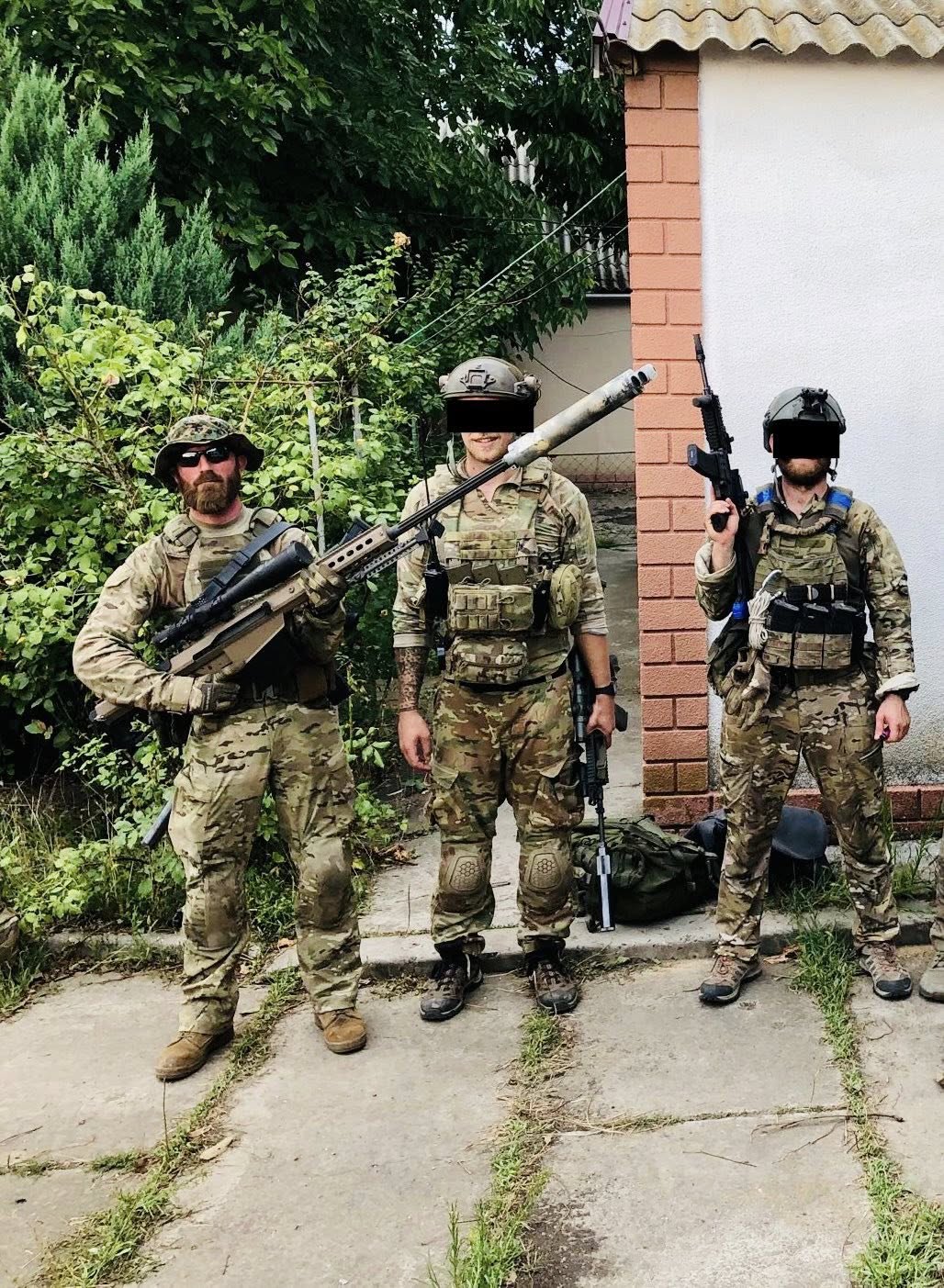 Three operators in multicam combat fatigues with rifles standing in a yard; two of the three faces are redacted.